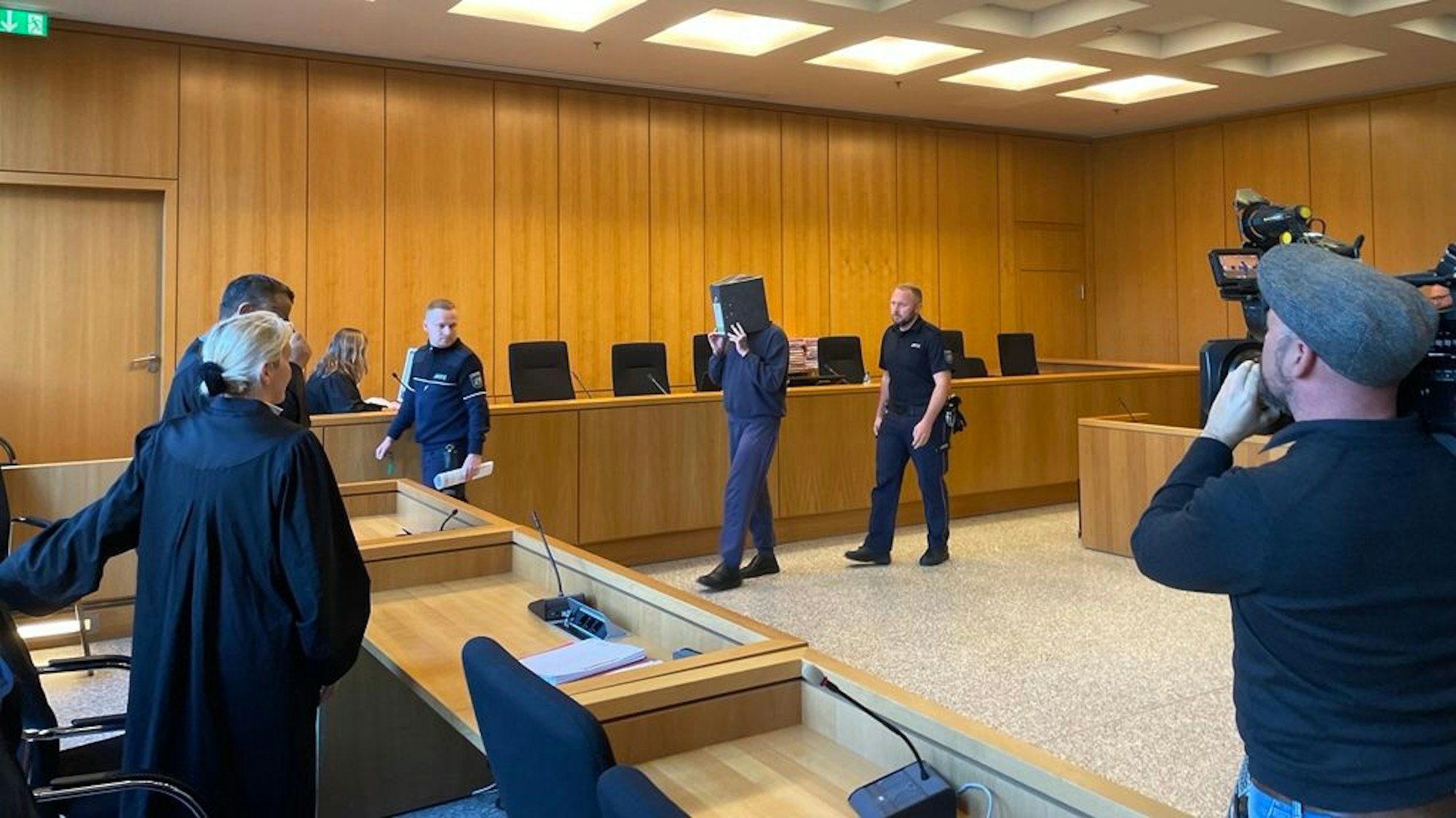 Der ehemalige Krankenpfleger, der wegen zehnfachen Mordes und 27-fachen Mordversuchs zu einer lebenslangen Freiheitsstrafe verurteilt wurde, verbirgt sein Gesicht hinter einem Aktenordner, als er in den Verhandlungssaal am Landgericht Aachen geführt wird.