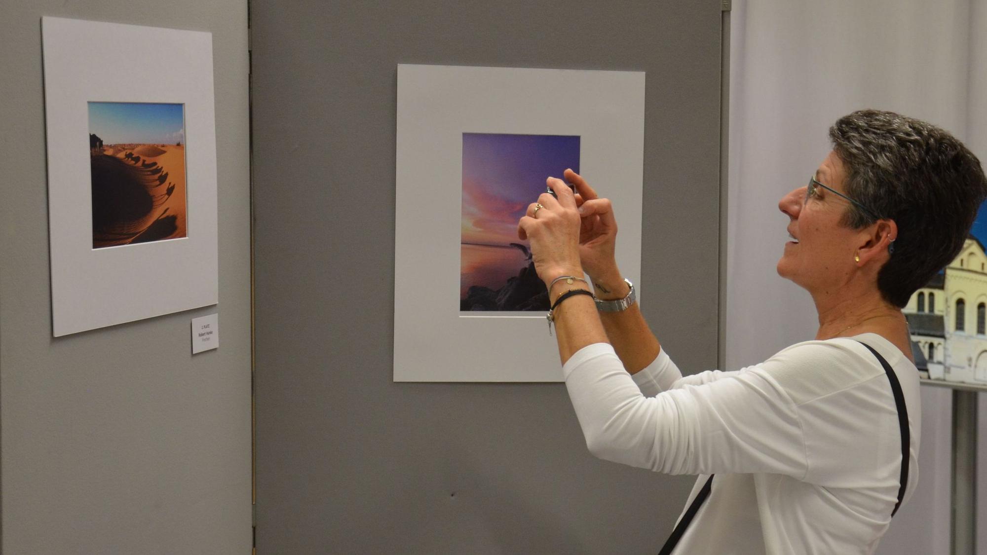 Zu sehen ist eine Frau, die eine Aufnahme von einem ausgestellten Foto macht.