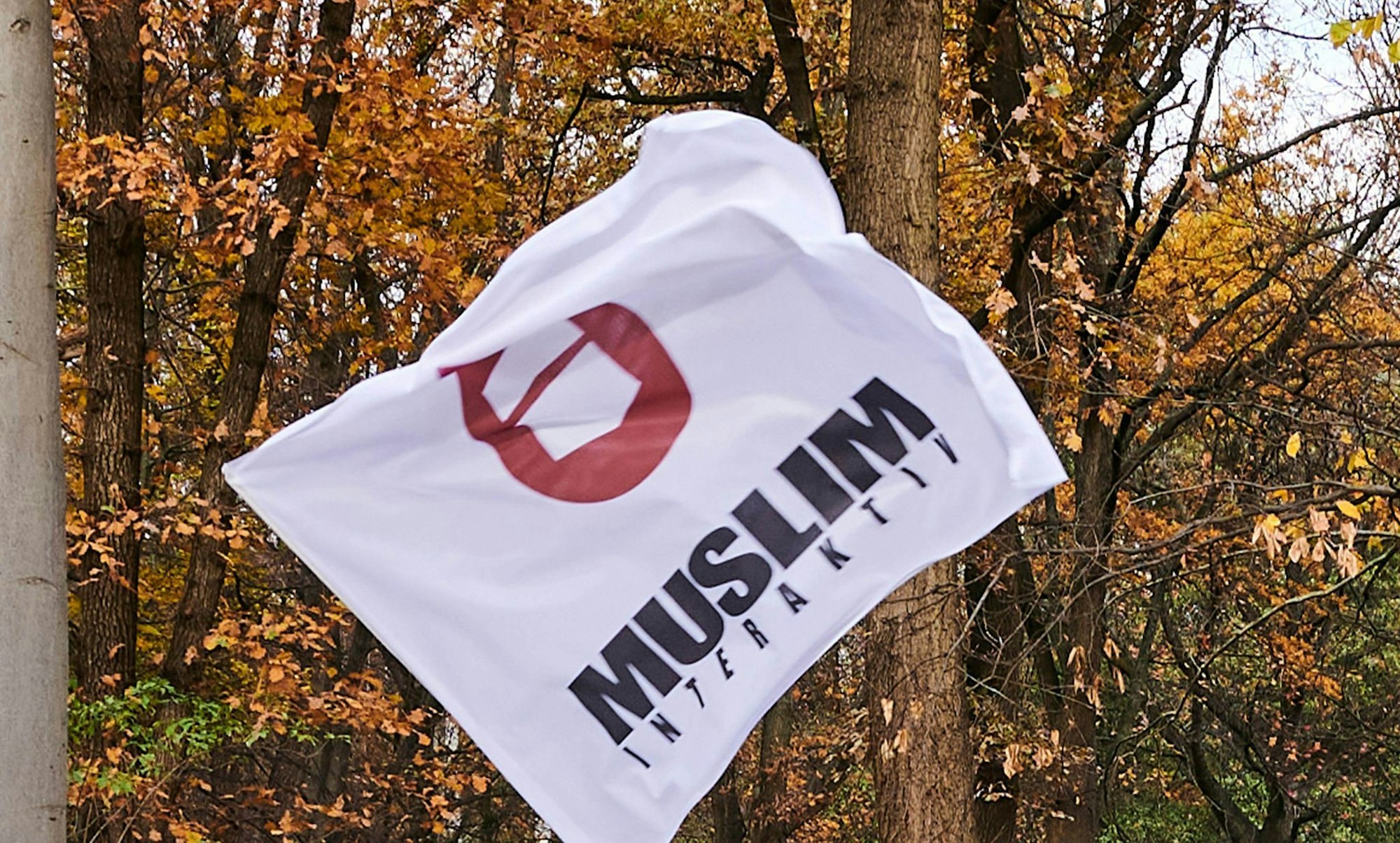 Eine Fahne mit dem Logo von Muslim Interaktiv weht vor einem Baum. (Symbolbild)