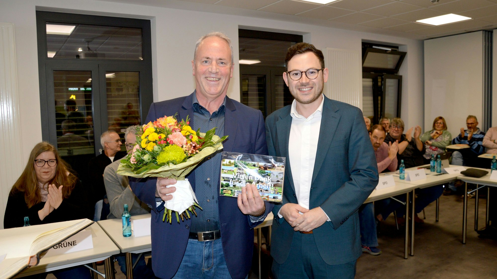 Hermann-Josef Esser (l.) hält einen Blumenstrauß und ein Präsent in den Händen, Emmanuel Kunz steht neben ihm.