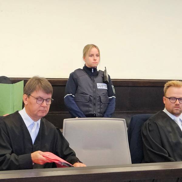 Ein Angeklagter sitzt mit einem Aktendeckel vor dem Gesicht auf der Anklagebank des Paderborner Landgerichts.
