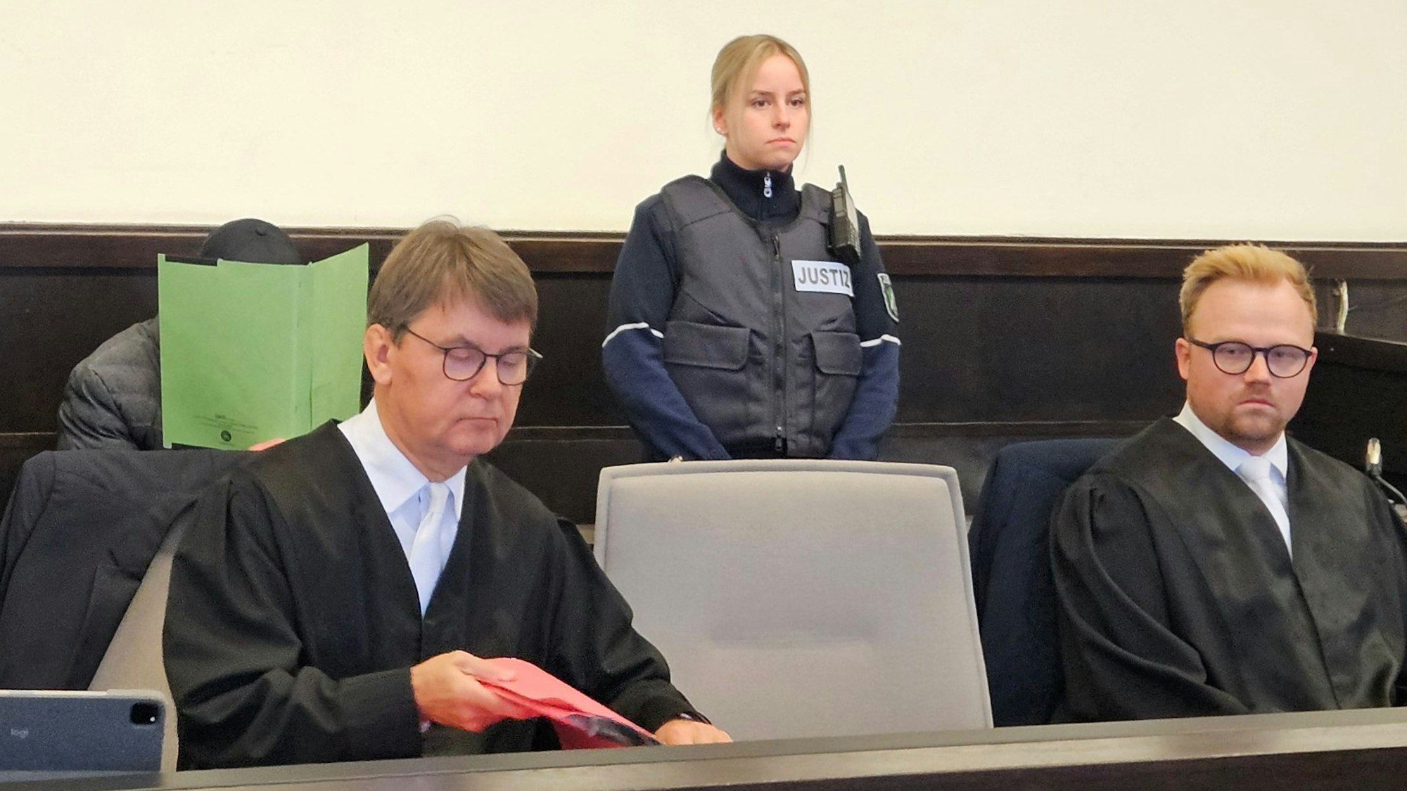 Der Angeklagte sitzt im Gerichtssaal und hält sich eine grüne Mappe vor das Gesicht.