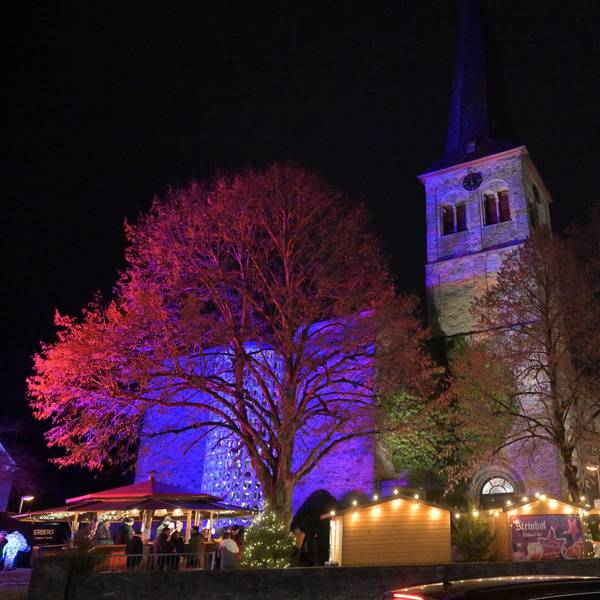Der Overather Weihnachtsmarkt und die angestrahlte Kirche St. Walburga am Abend.
