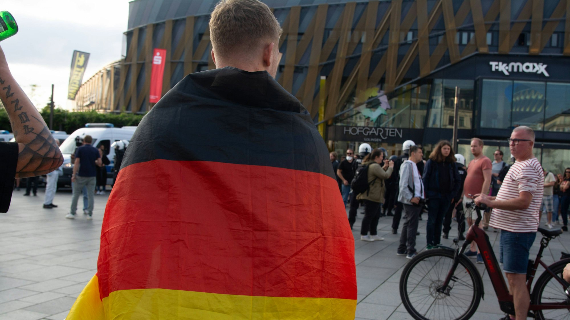 Ein junger Mann steht auf einem Platz in Solingen, um die Schultern hat er sich eine Deutschlandfahne geschwungen.