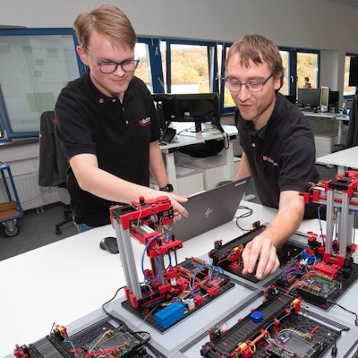 Zwei junge Männer fassen an eine Fischer-Technik-Anlage.