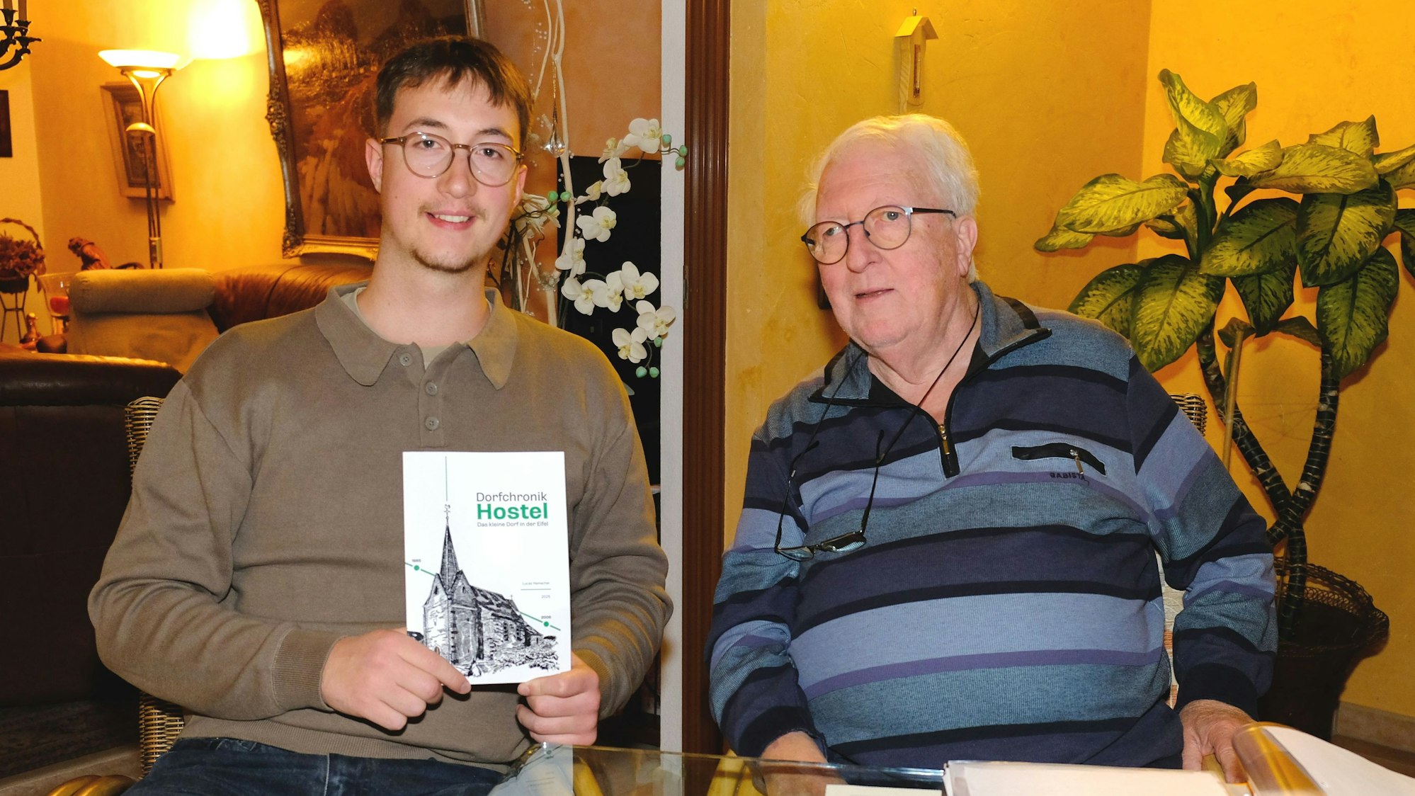 Der 23-jährige Lucas Hamacher (l.) hält die von ihm verfasste Dorfchronik von Hostel in Händen, neben ihm sitzt sein Großvater Dieter Schröder.