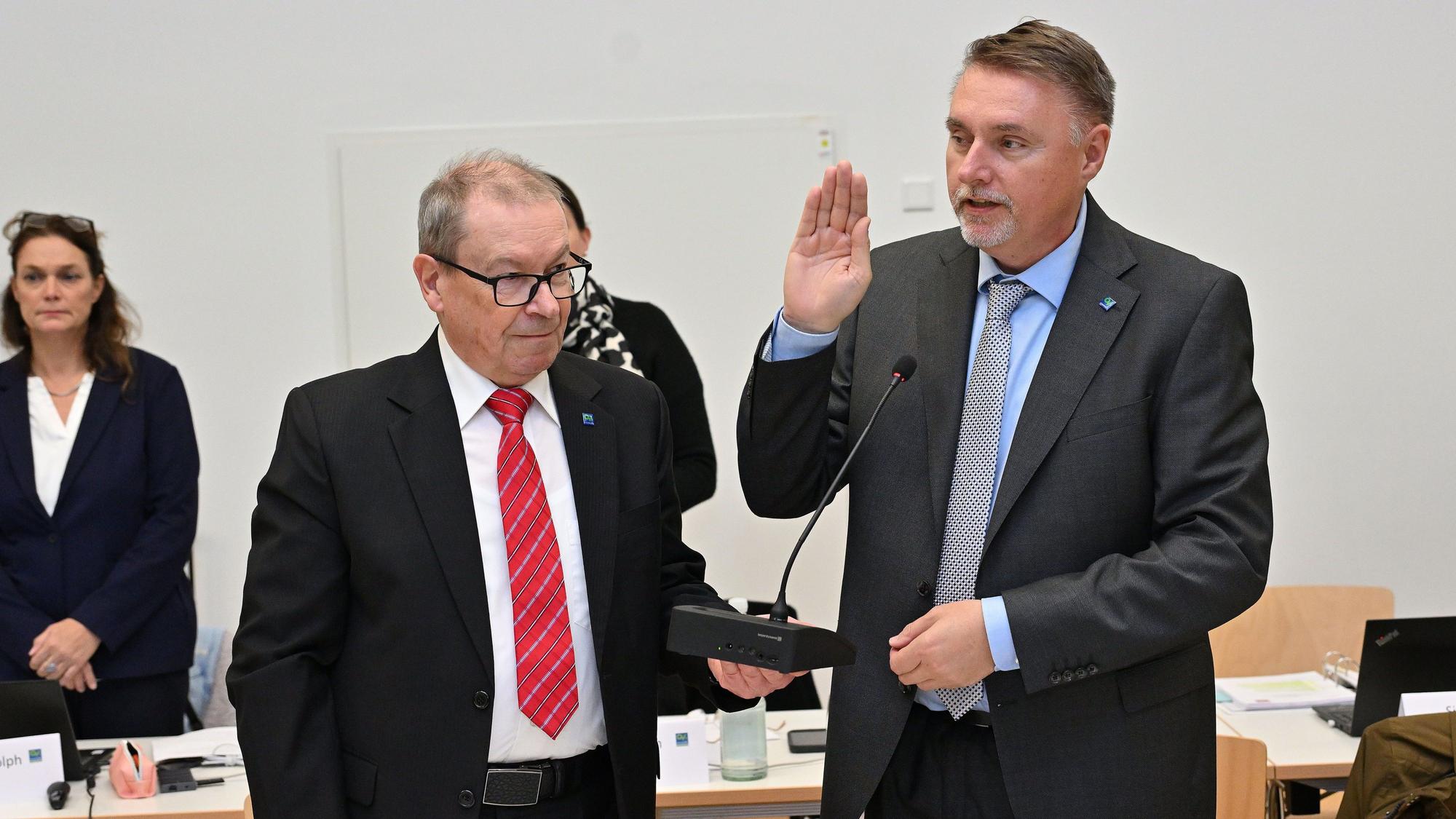 Zwei Männer stehen nebeneinander, einer hat die Hand gehoben, um einen Eid abzulegen.