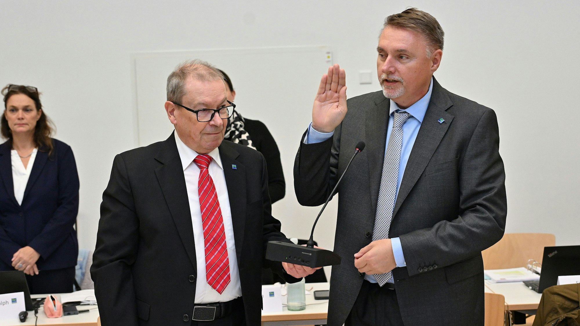 Zwei Männer stehen nebeneinander, einer hat die Hand gehoben, um einen Eid abzulegen.