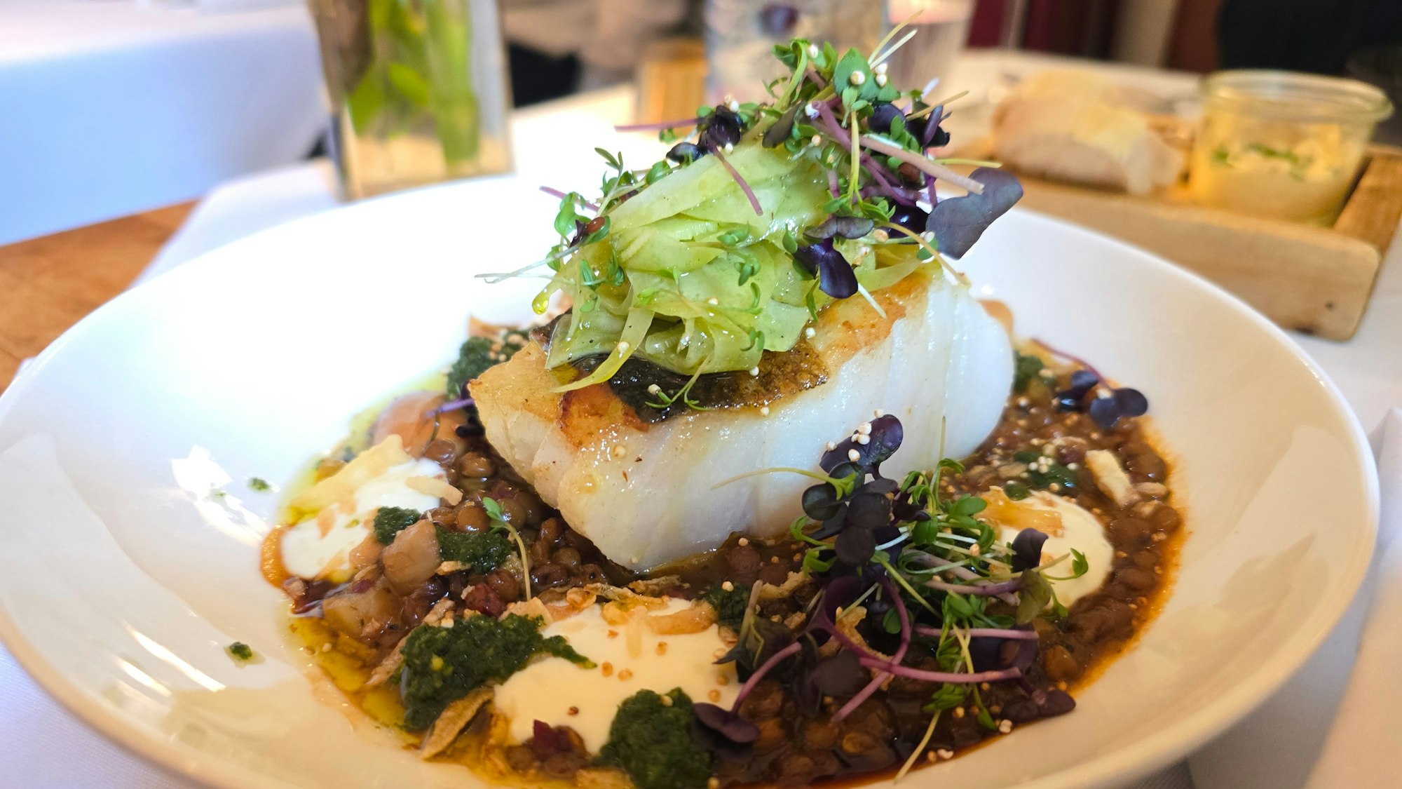 Tellergericht mit einem dicken weißen Fischfielt auf Linsen, mit Salat und Sprossen dekoriert.