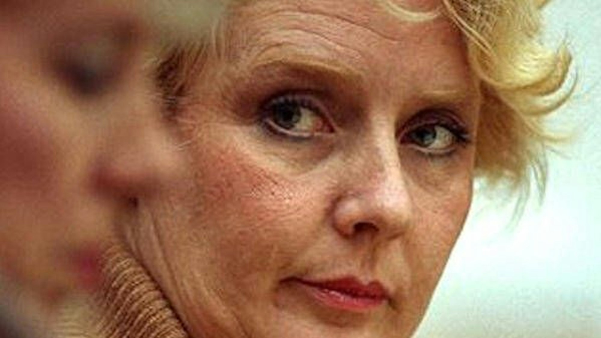 Betty Broderick mit blonden Haaren, die aufmerksam seitlich blickt