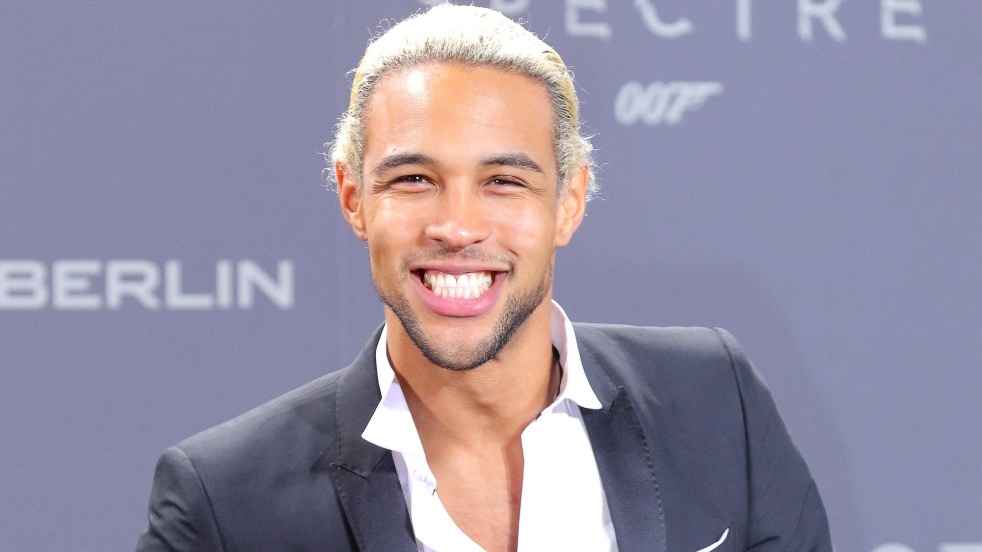 Simon Desue lacht bei einem Event auf dem roten Teppich.