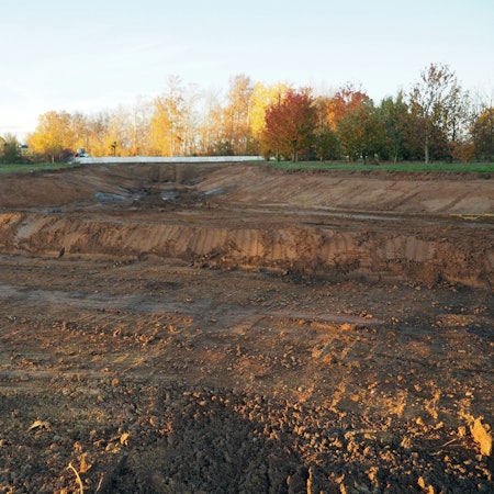 Im Vordergrund befindet sich der ausgehobene Graben, im Hintergrund stehen Bäume.