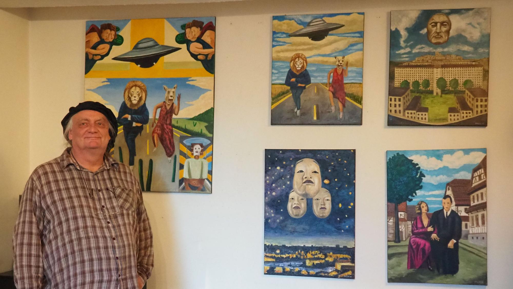 Michael Münch steht vor einer Wand, an der seine Bilder hängen.