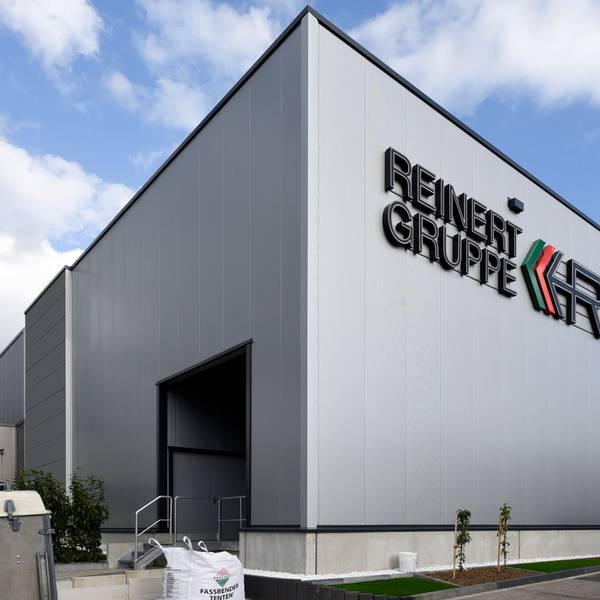 Zu sehen ist eine graue Lagerhalle vor blauem Himmel mit der Aufschrift „Reinert Gruppe“.