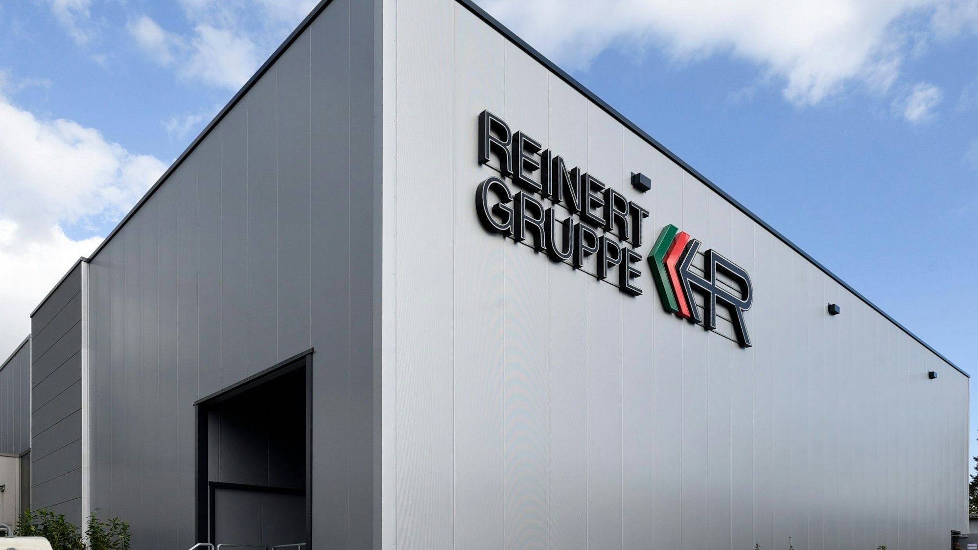 Zu sehen ist eine graue Lagerhalle vor blauem Himmel mit der Aufschrift „Reinert Gruppe“.