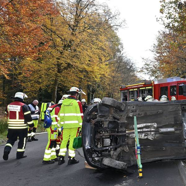Ein Auto liegt auf der Seite auf der Straße, darum herum Feuerwehrleute.