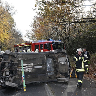 Ein Auto liegt auf der Seite auf der Straße, darum herum Feuerwehrleute.