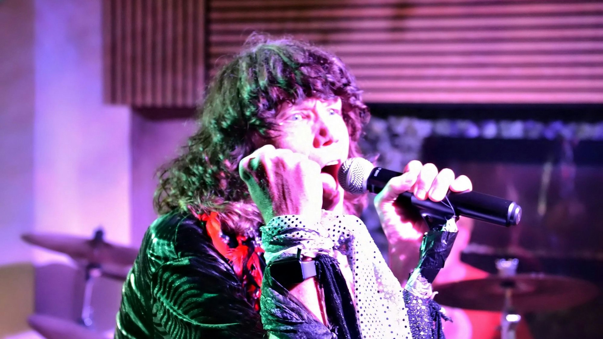Der Sänger der Band trägt eine grüne Glitzerjacke.