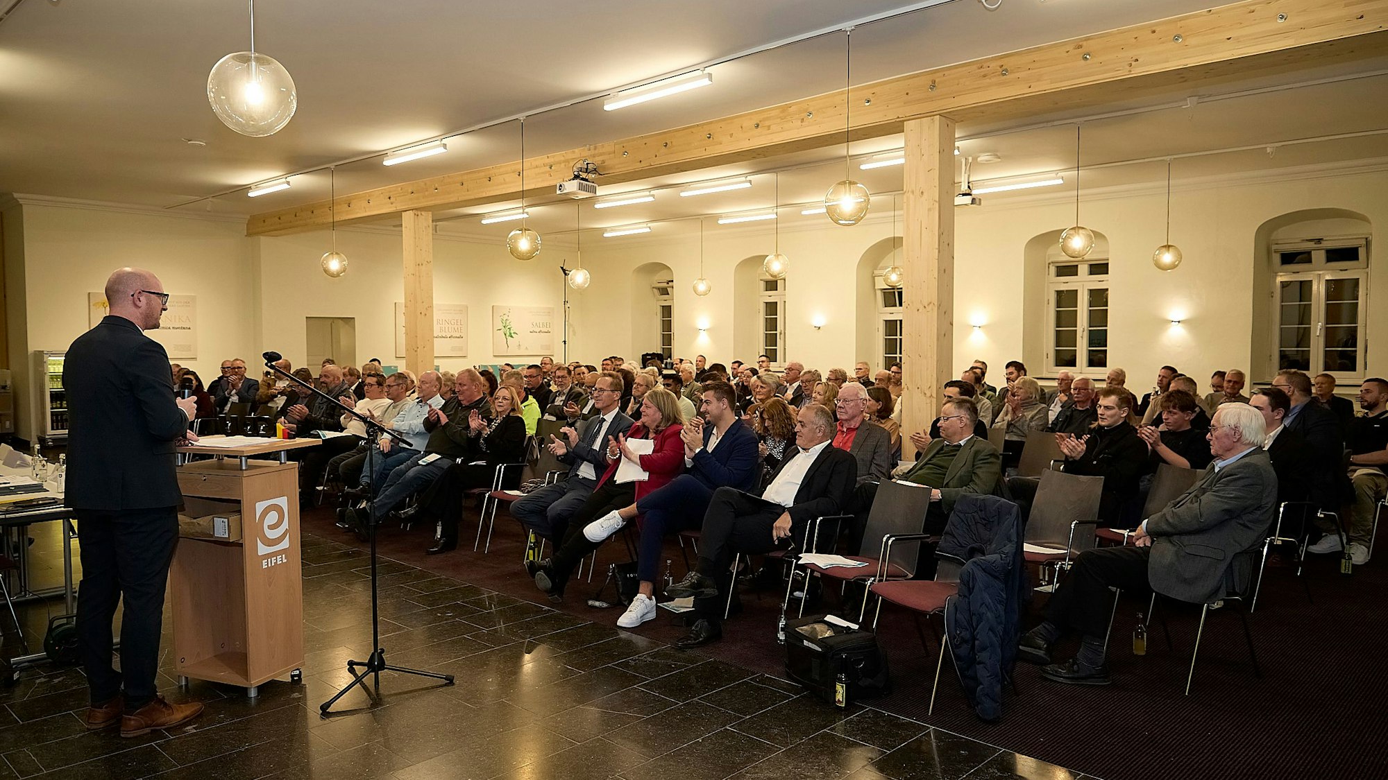 Pfennings steht am Mikrofon, seine Zuhörerinnen und Zuhörer sitzen in Stuhlreihen.