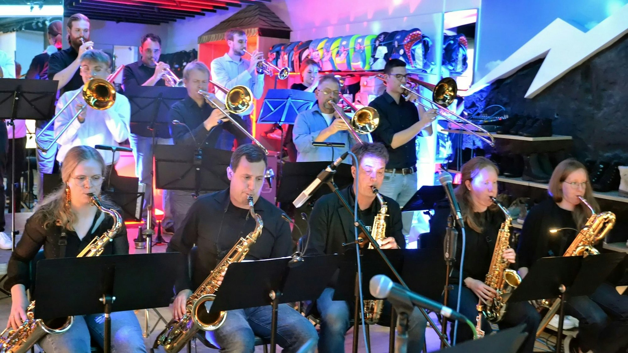 In der ersten Reihe sitzen Musikerinnen und Musiker mit Saxofon, dahinter stehen Posaunisten und Trompeter.