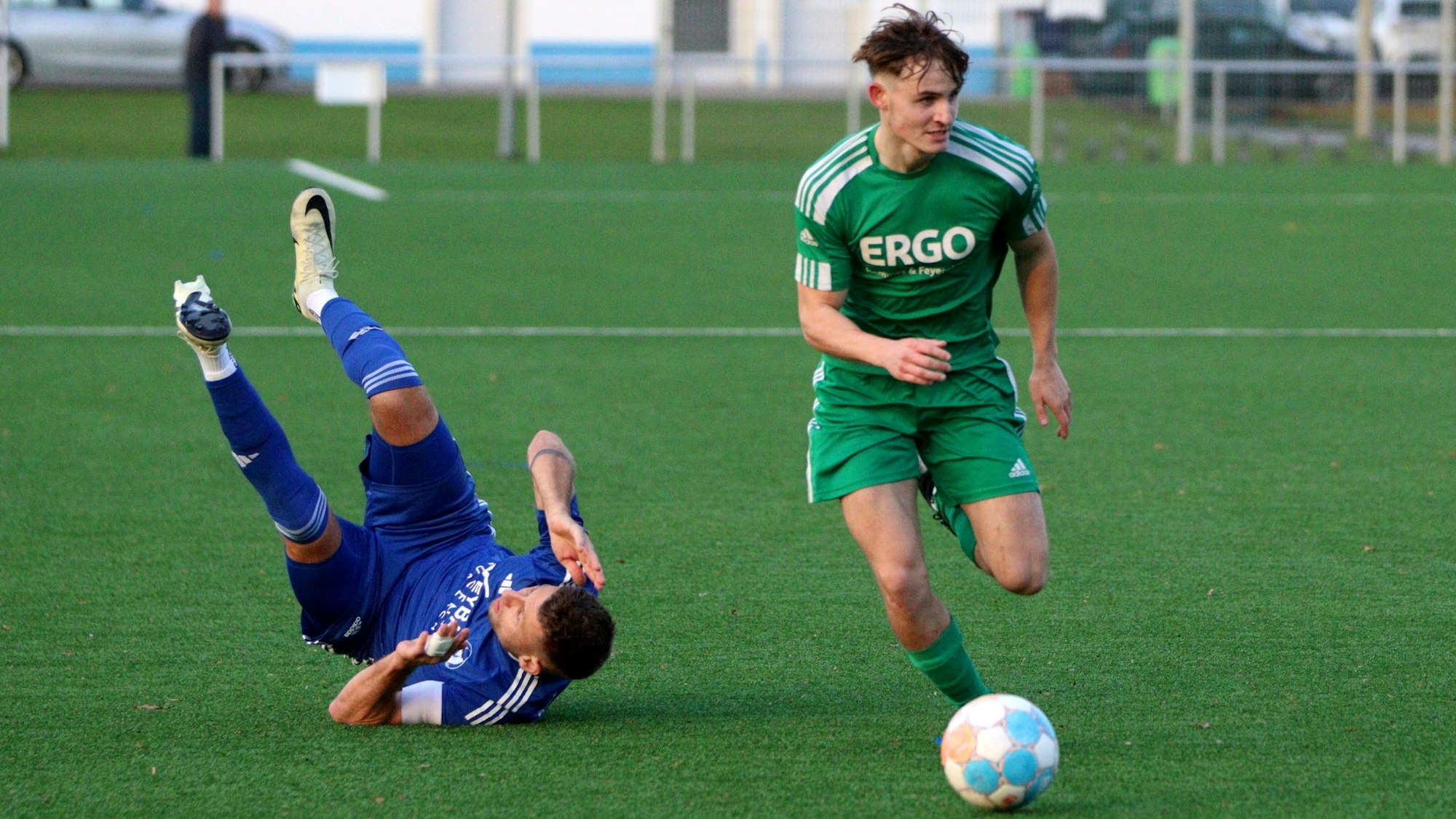 Ben Winter am Ball, hinter ist Kai Karamouzas gestürzt und liegt, mit in die Höhe gestreckten Beinen, auf dem Rücken.