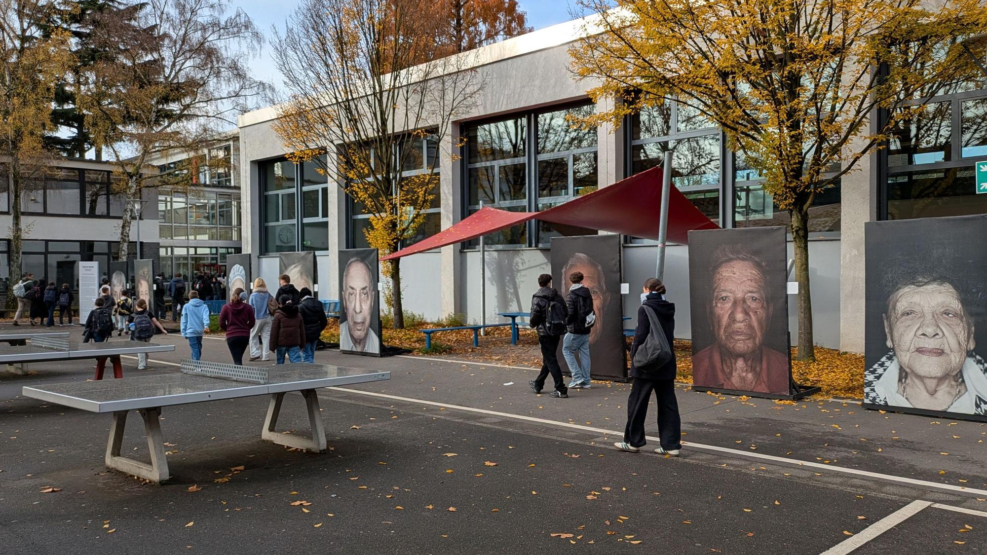 Schüler gehen an großformatigen Porträtfotos auf einem Schulhof vorbei.