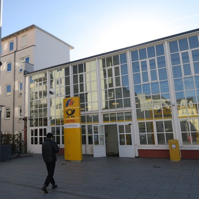 Ein Mann geht auf den Eingang einer Postbank-Filiale zu, die eine große Fensterfront hat.