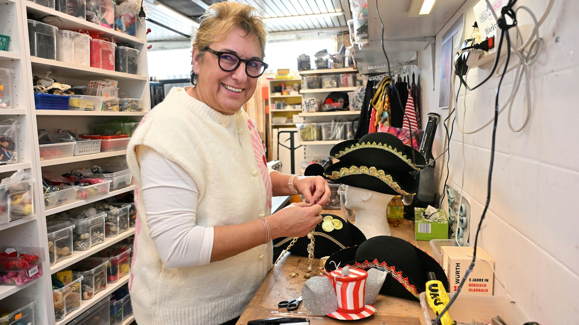 Eine Frau (Brigitte Meyer) steht hinter einer Werkbank auf der Piratenhüte liegen. Im Hintergrund ist Bastelmaterial zu sehen.