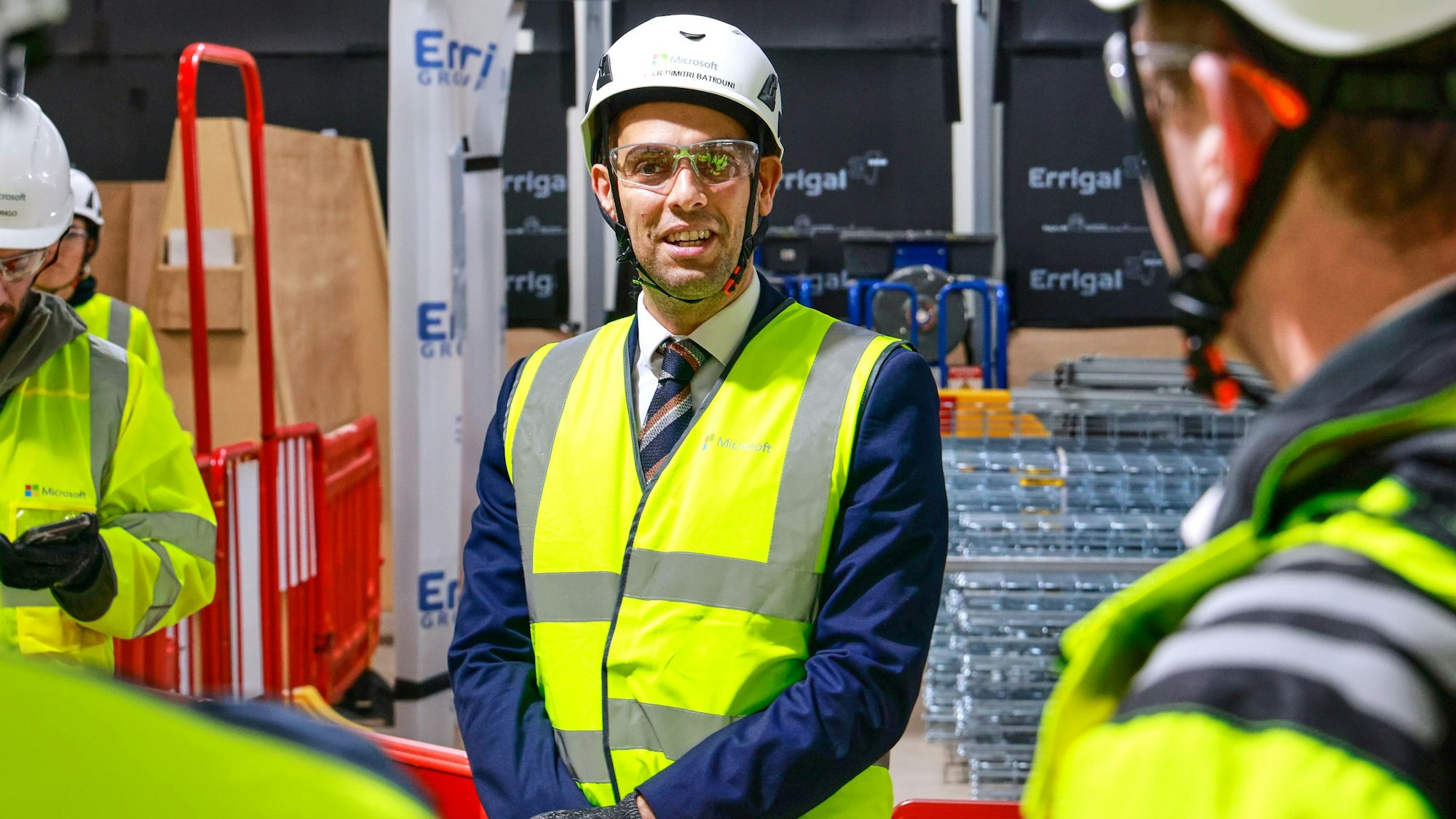 Ein Mann steht in Warnweste und Helm auf einer Baustelle.