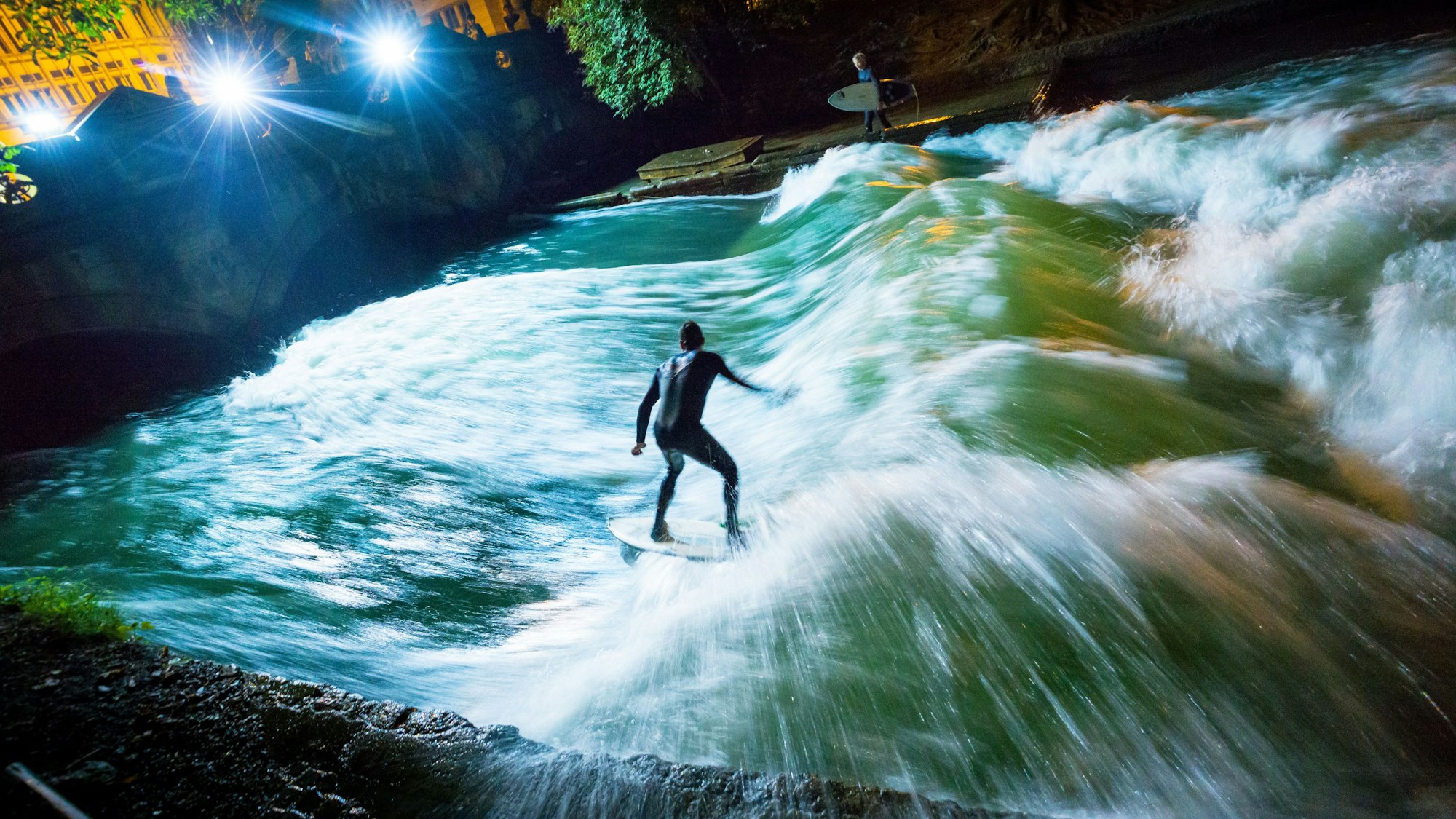 Ein Surfer reitet bei Nacht mit seinem Board über die künstliche Welle des Eisbachs im Englischen Garten.(