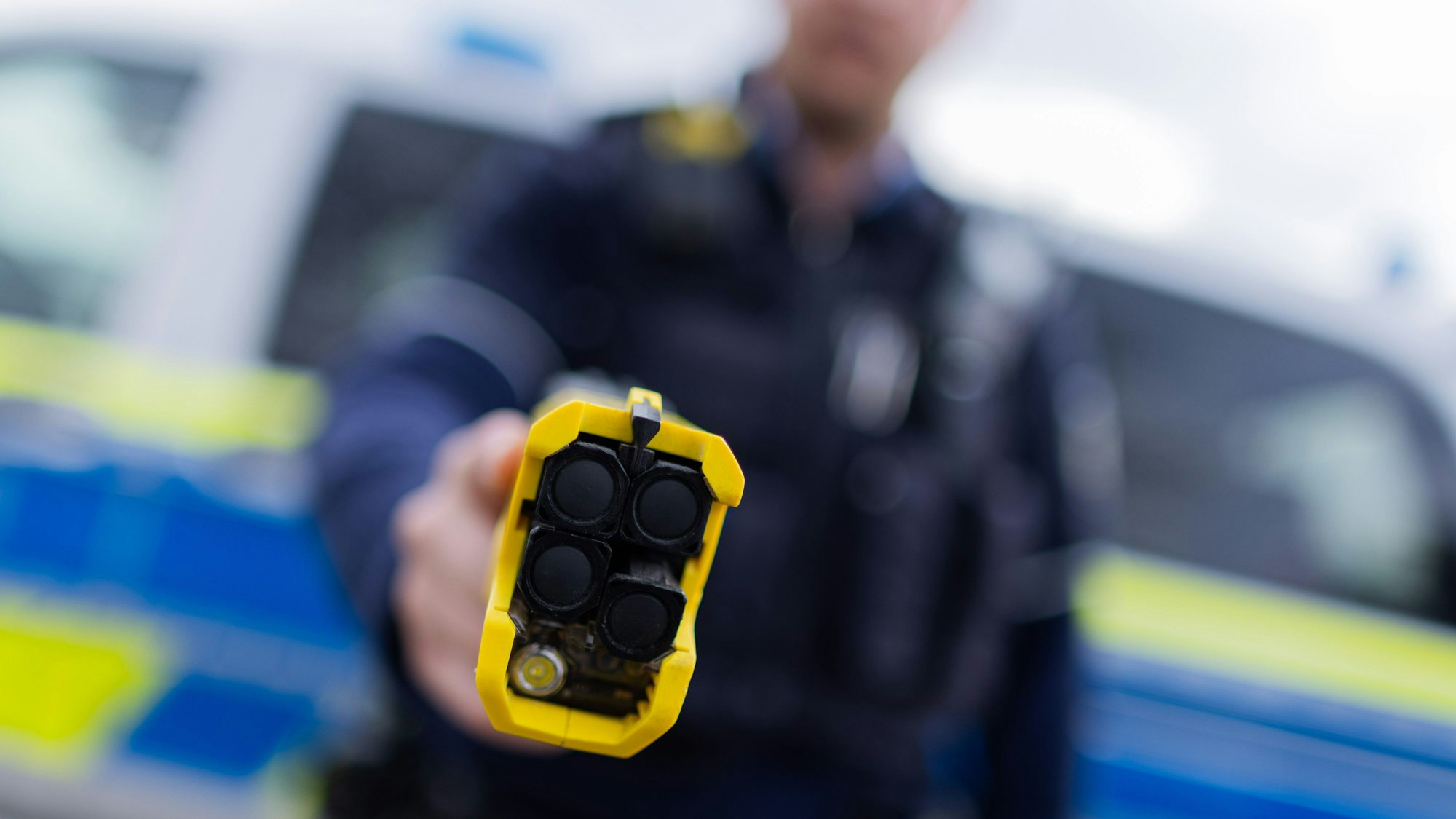 Ein Polizist hält einen Taser (Distanzelektroimpulsgerät) in den Händen. Das Gerät sendet nach Abschuss zweier Elektroden Stromimpulse ab.