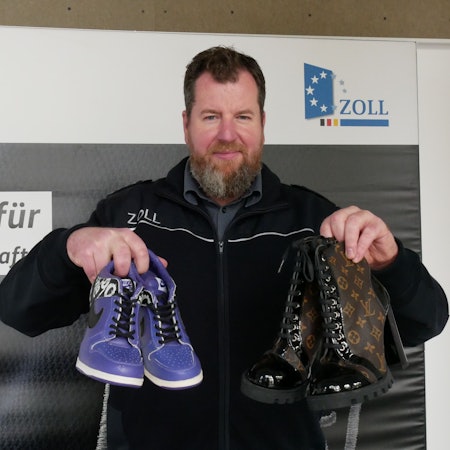Zoll-Sprecher Jens Ahland hält gefälschte Schuhe in Händen.