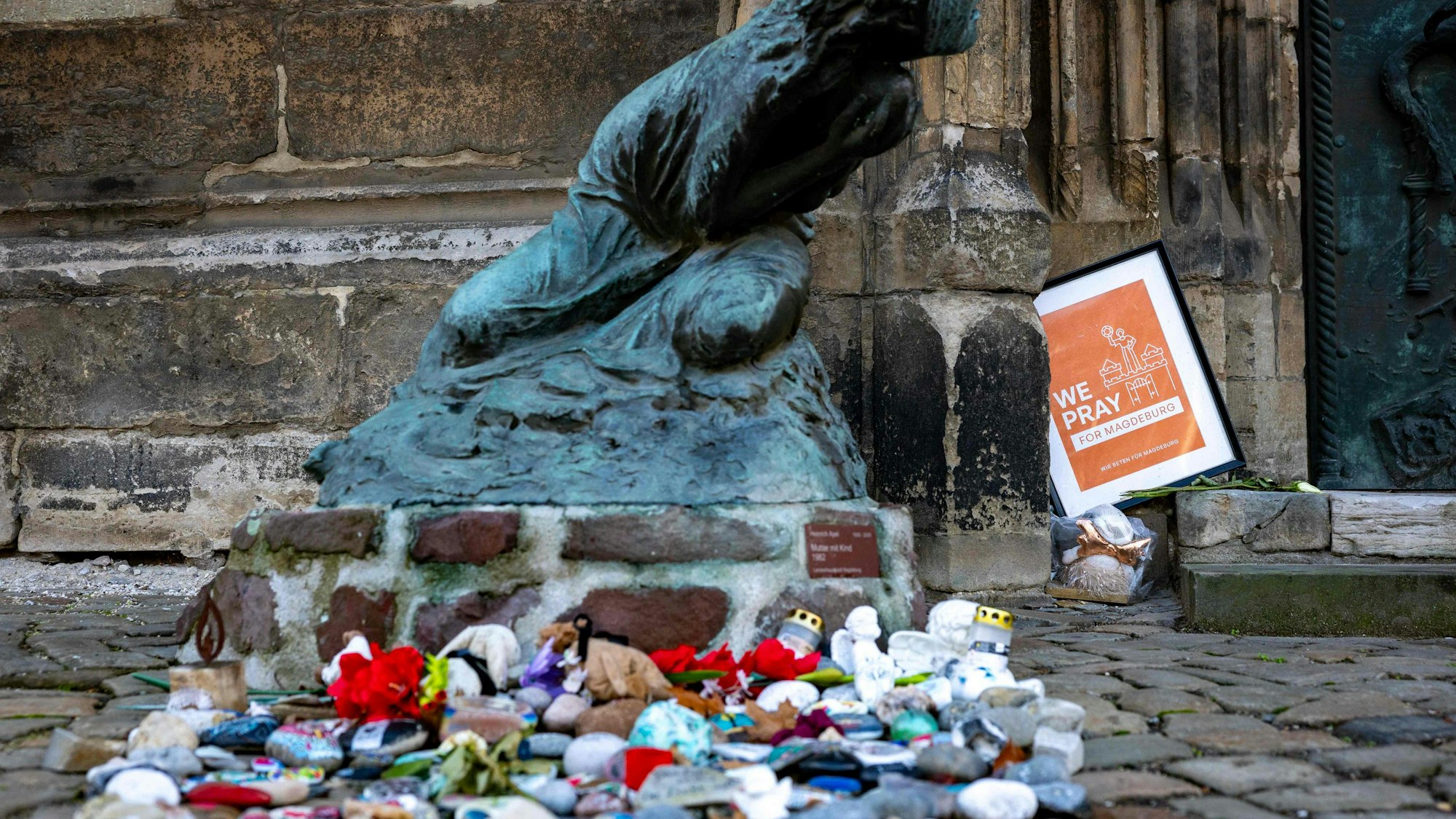 Blumen und Kerzen zum Gedenken an die Opfer des Anschlags auf den Weihnachtsmarkt 2024 liegen vor der Johanniskirche in Magdeburg.
