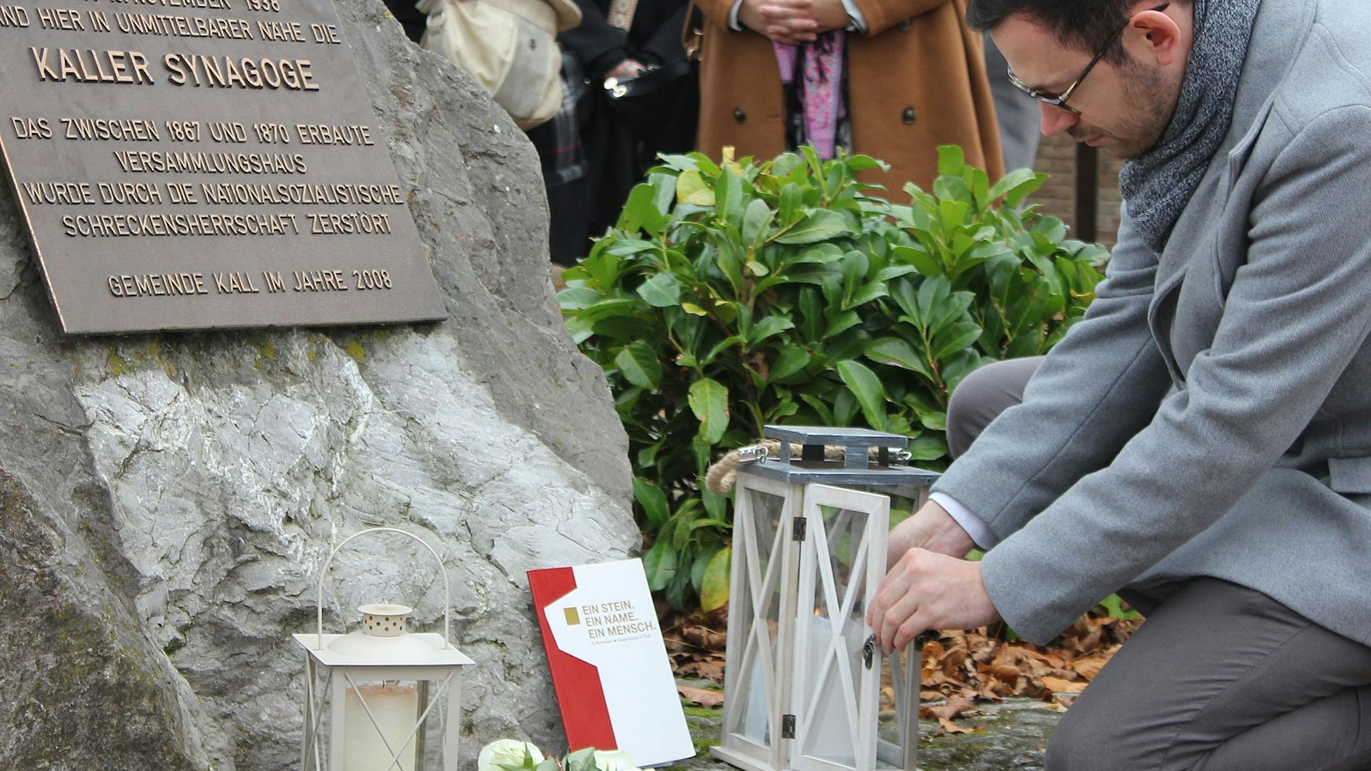 Bürgermeister Kunz kniet vor der Gedenktafel und zündet eine Kerze an.