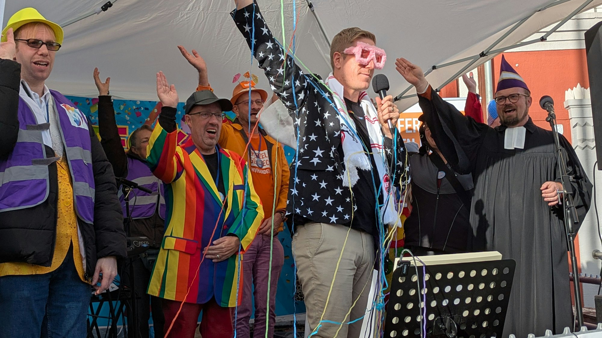 Markus Ramers, der eine rosa-jecke Brille trägt, ruft von der Bühne aus „Alaaf“.