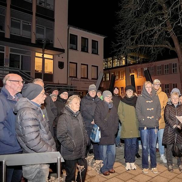 Am Mahnmal in Schleiden stehen Teilnehmende der Gedenkveranstaltung und hören F.A. Heinen bei seiner Rede zu.