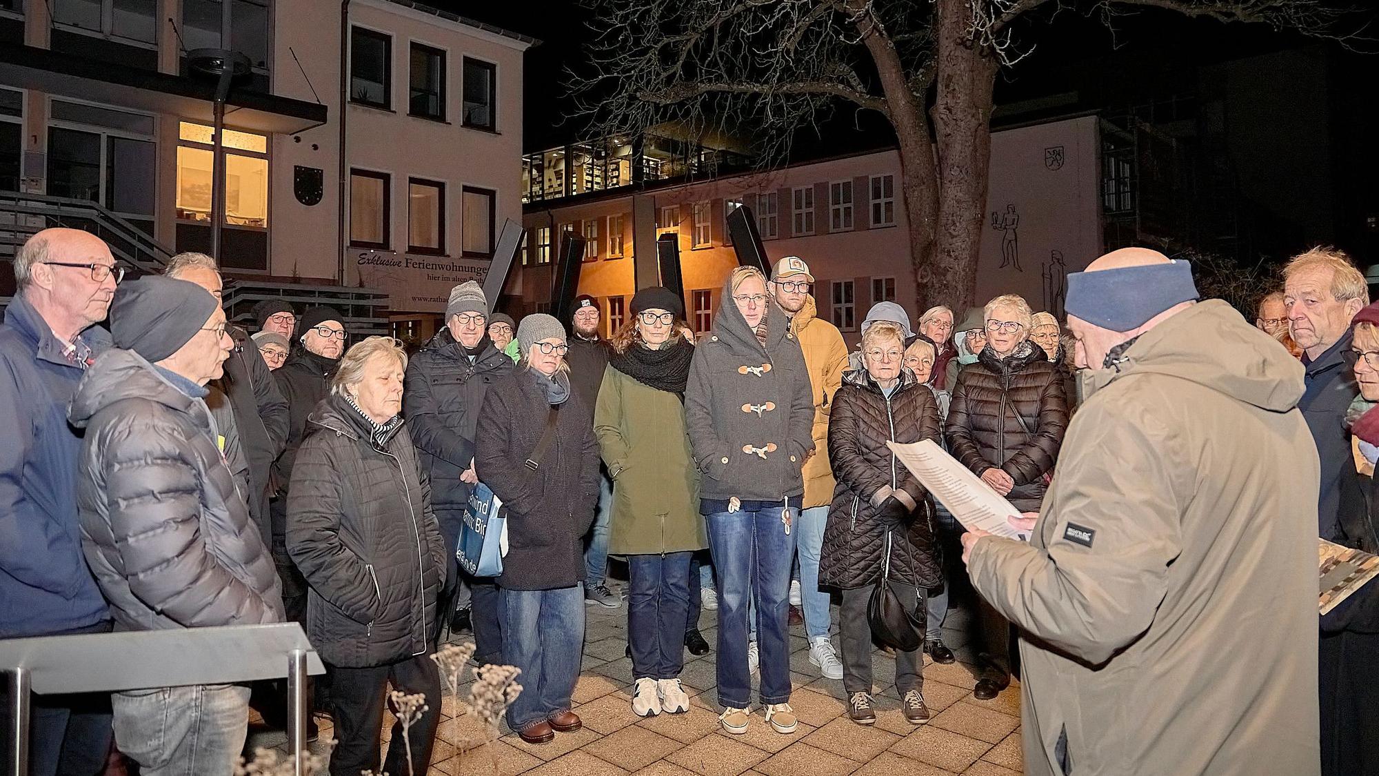 Am Mahnmal in Schleiden stehen Teilnehmende der Gedenkveranstaltung und hören F.A. Heinen bei seiner Rede zu.