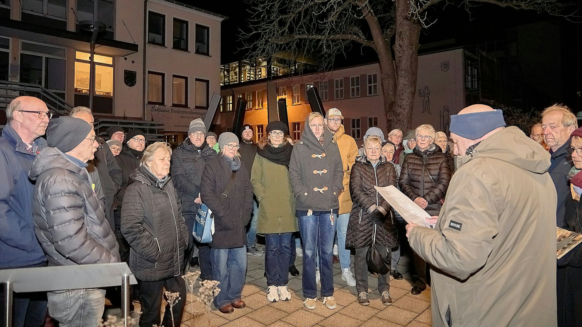 Am Mahnmal in Schleiden stehen Teilnehmende der Gedenkveranstaltung und hören F.A. Heinen bei seiner Rede zu.