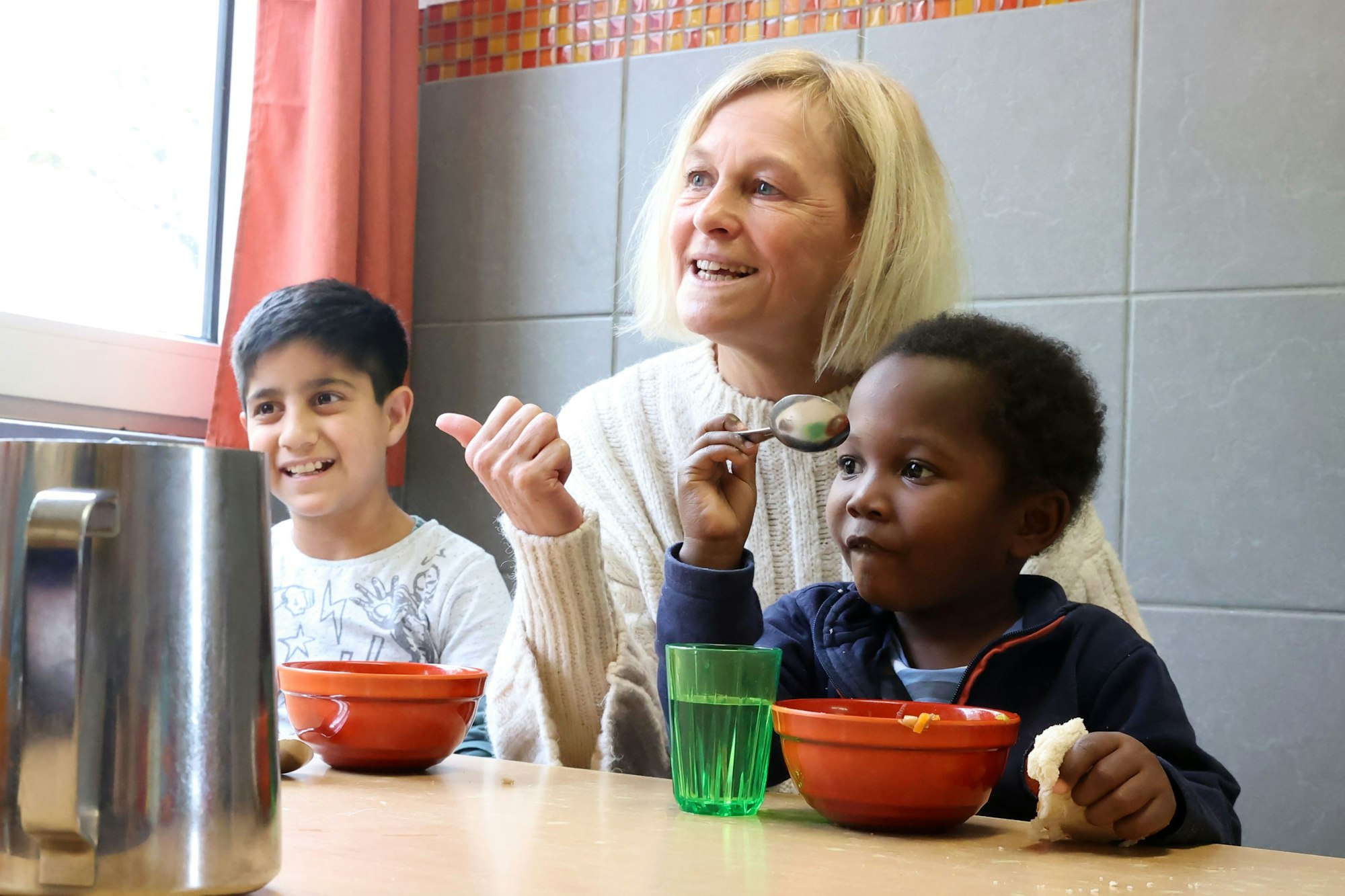Farid aus Afghanistan sowie Stelvio aus Angola sitzen mit Claudia Peppmüller am Esstisch.