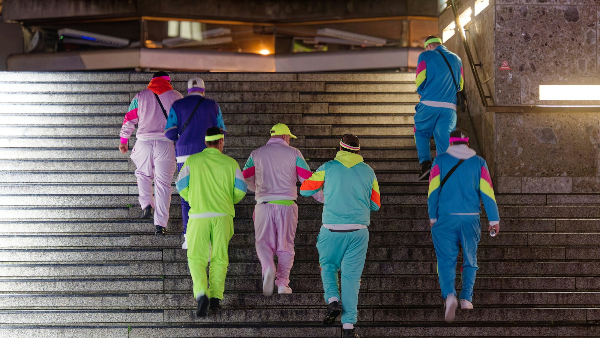 Diese Gruppe junger Männer schreitet in neonfarbenen Trainingsanzügen in Richtung Kölner Altstadt.