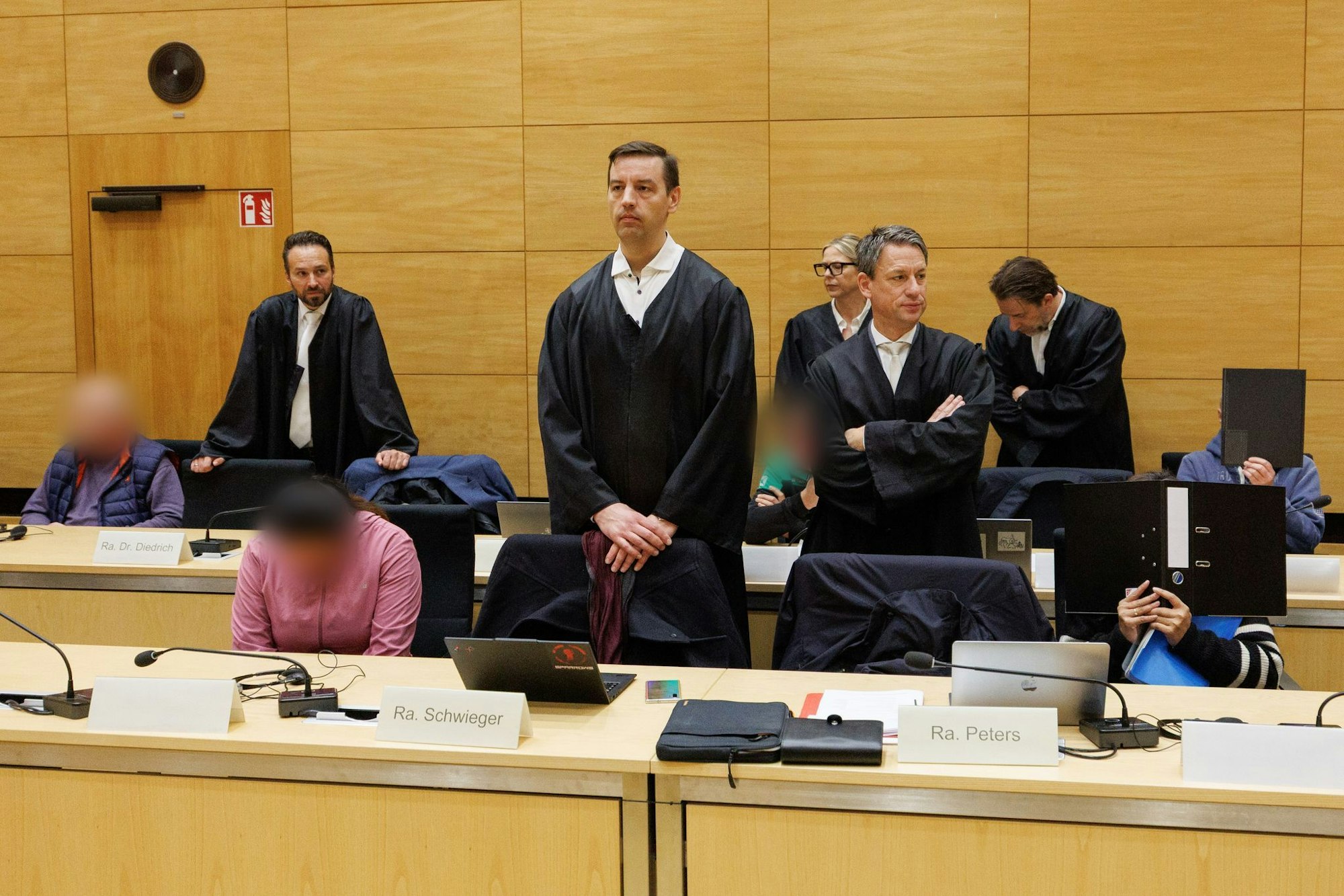 Drei der zehn Angeklagten sitzen am ersten Prozesstag im Landgericht Bielefeld neben ihren Verteidigern.