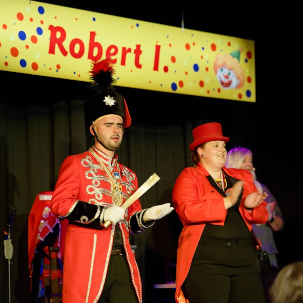 Robert Herter trägt eine rote Uniform, neben ihm steht eine ebenfalls rot gekleidete Frau.