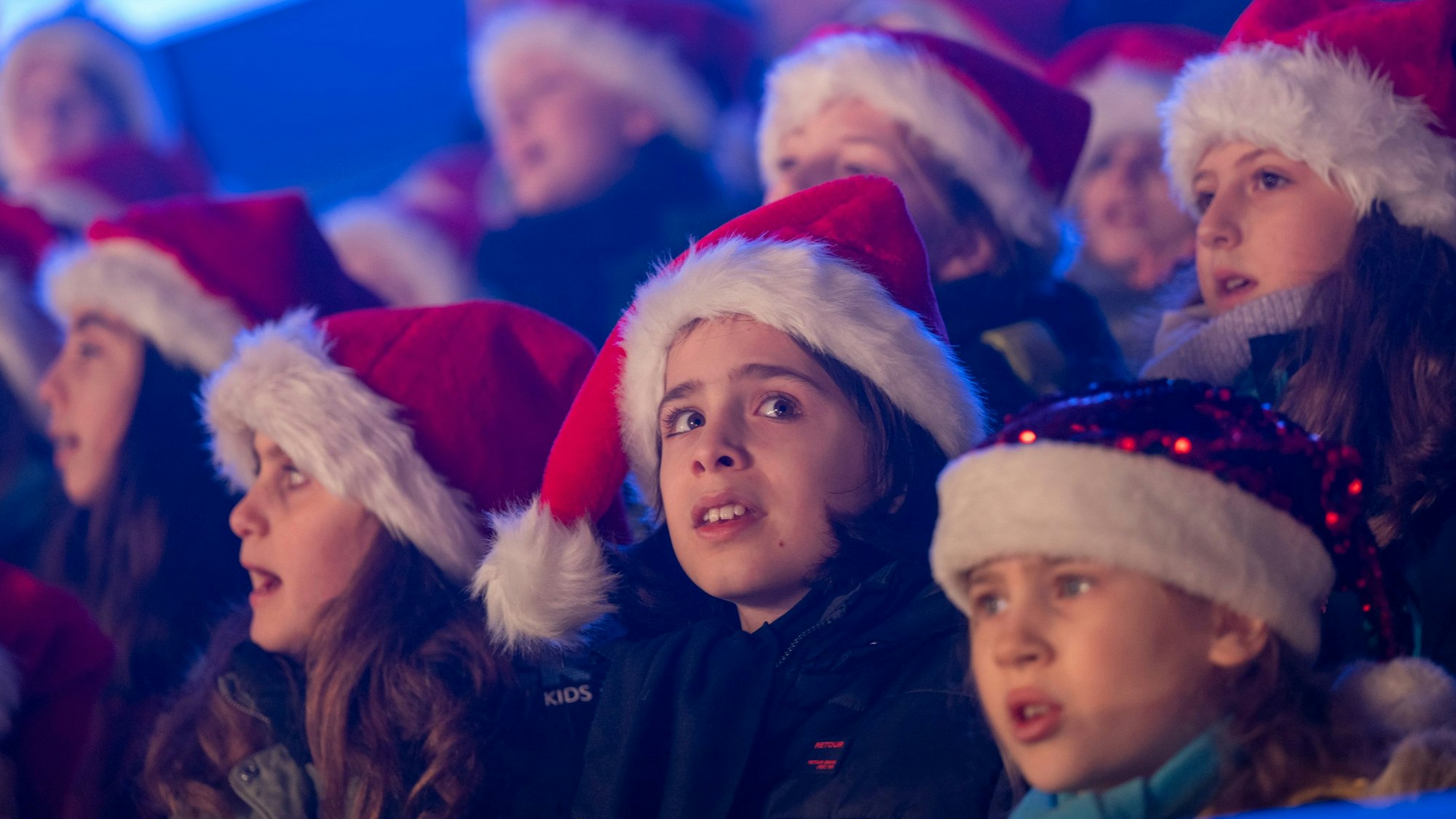 Kinder mit Weihnachtsmützen singen.