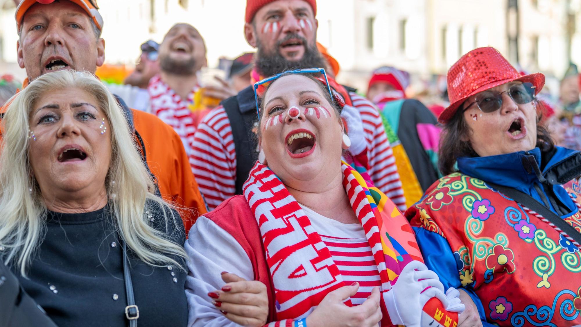 Fünf Menschen in bunten Kostümen schunkeln eingehakt und singen.