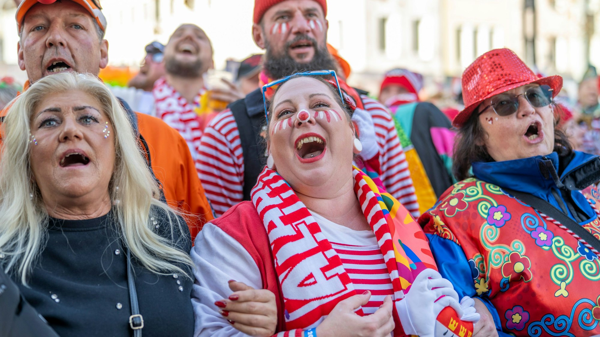 Fünf Menschen in bunten Kostümen schunkeln eingehakt und singen.