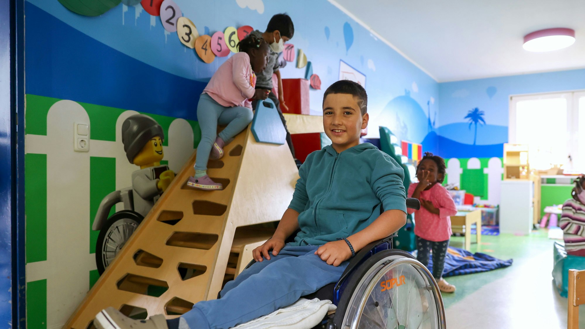 Gul Ahmad aus Afghanistan
ist im Spielzimmer in seinem Rollstuhl zu sehen. Er lächelt in die Kamera.
