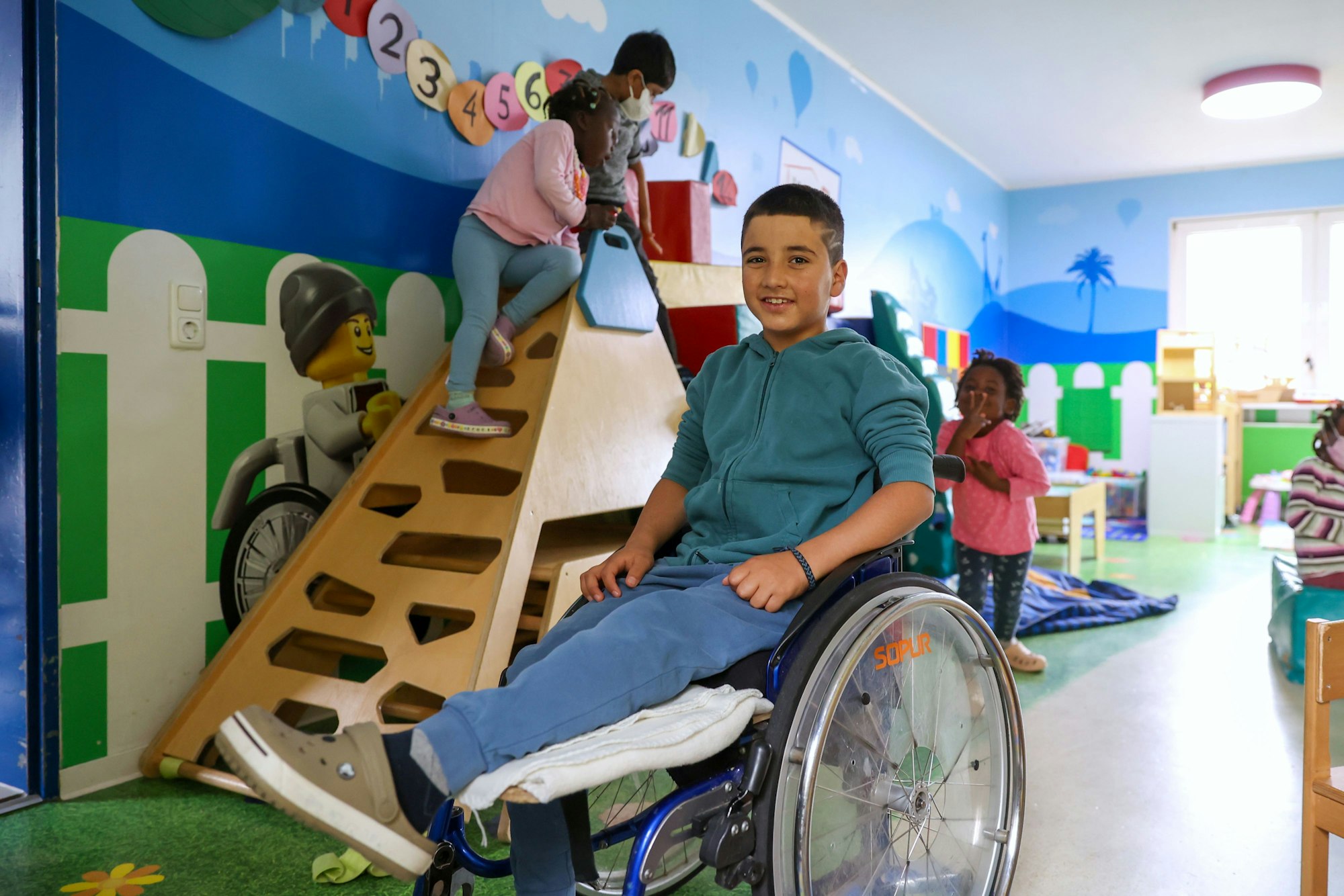 Gul Ahmad aus Afghanistan
ist im Spielzimmer in seinem Rollstuhl zu sehen. Er lächelt in die Kamera.