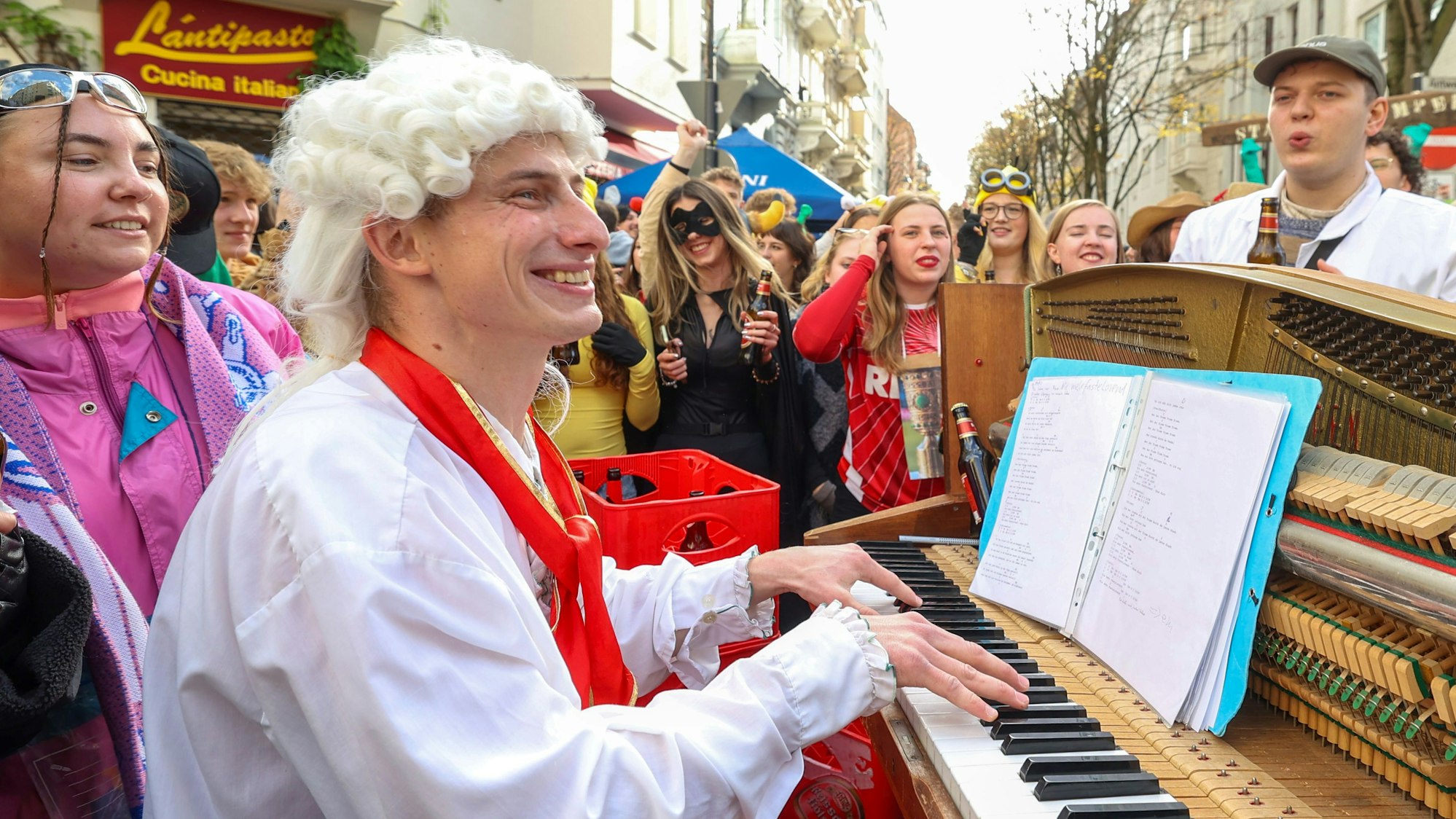 Der Musiker spielt auf einem Klavier auf der Straße, umringt von verkleideten Personen.