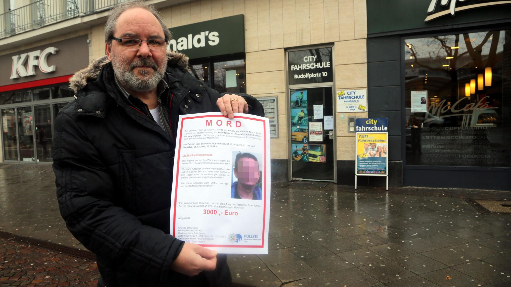 Ein Mitarbeiter der Mordkommission zeigt im Februar 2013 ein Fahndungsplakat, mit dem der Mörder von Helmut B. gesucht wird. Im Haus dahinter geschah das Verbrechen.