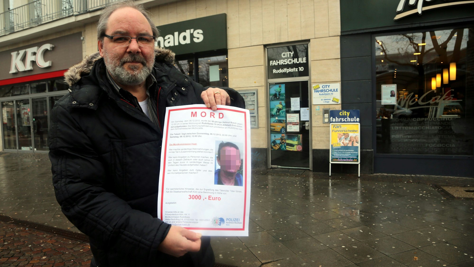 Ein Mitarbeiter der Mordkommission zeigt im Februar 2013 ein Fahndungsplakat, mit dem der Mörder von Helmut B. gesucht wird. Im Haus dahinter geschah das Verbrechen.